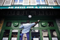 A cafe employee, Djibril, cleans the front window of a closed cafe, in Paris, Monday, June 1, 2020. Parisians who have been cooped up for months with take-out food and coffee will be able to savor their steaks tartare in the fresh air and cobbled streets of the City of Light once more -- albeit in smaller numbers. (AP Photo/Thibault Camus)