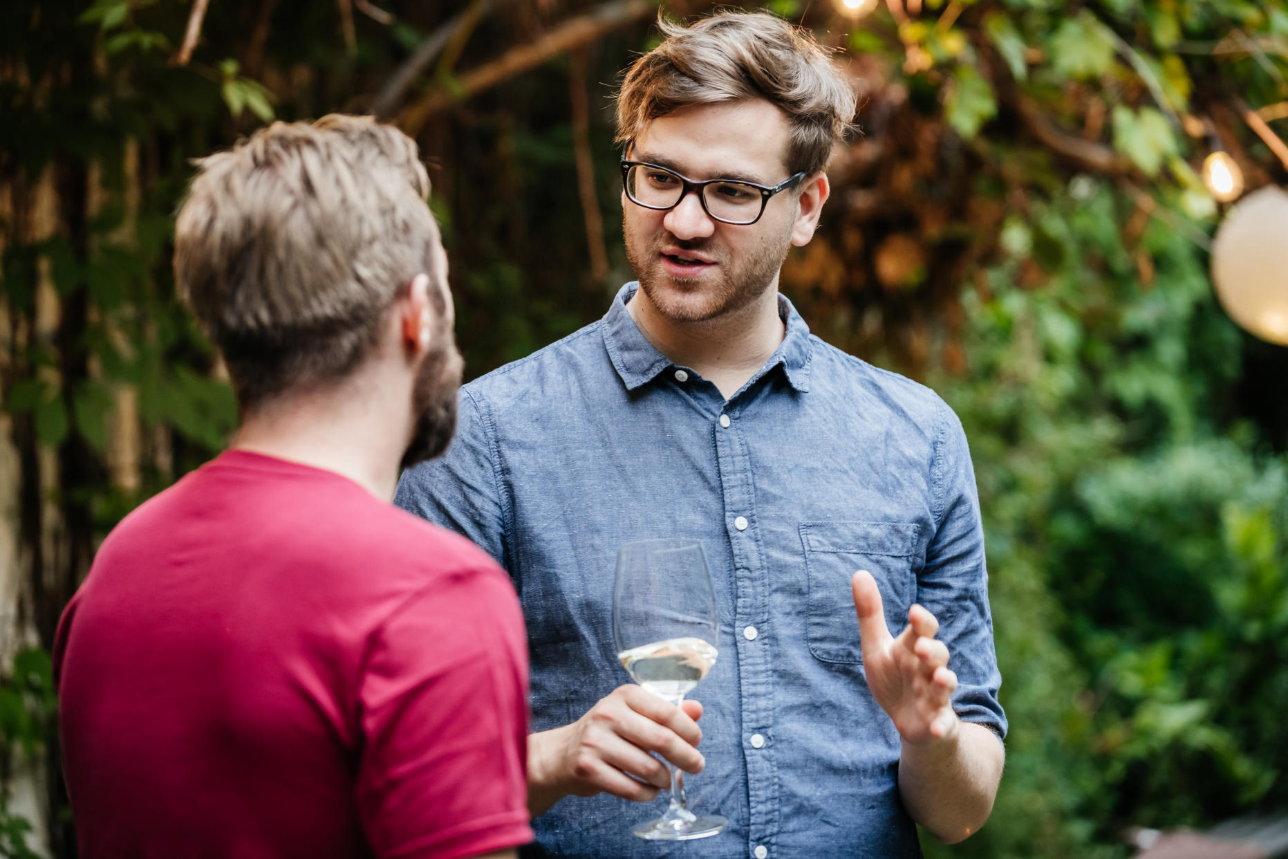 Two friends chatting and drinking with each other during a family barbecue in a courtyard.