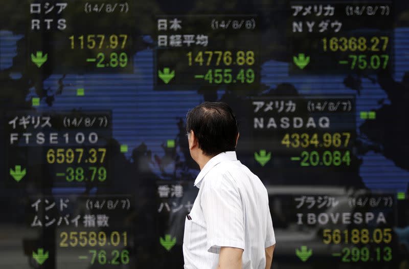 A pedestrian looks at an electronic board showing the stock market indices of various countries outside a brokerage in Tokyo August 8, 2014. REUTERS/Yuya Shino