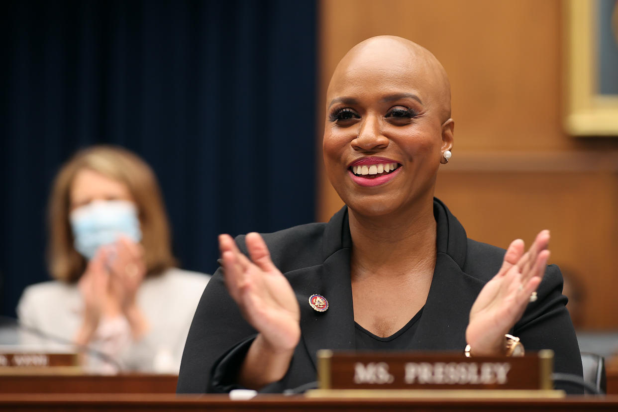 Ayanna Pressley smiles and applauds while seated behind a name plaque bearing her name.