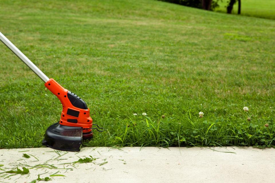 Person uses string trimmer to edge the lawn alongside a driveway.