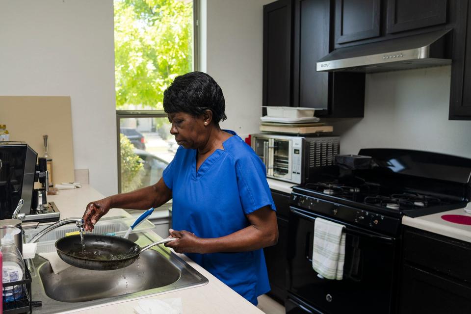 Shirley Eason washes dishes as she makes lunch while caring for Tommy Dang. “When she’s here, I try to eat as much as I can,” said Dang, a former sushi chef who, because of spinal cord injuries, can no longer cook for himself.