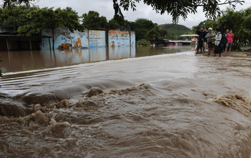 People stand on the edges of a flooded street after the passing of Iota in La Lima, Honduras, Wednesday, Nov. 18, 2020. Iota flooded stretches of Honduras still underwater from Hurricane Eta, after it hit Nicaragua Monday evening as a Category 4 hurricane and weakened as it moved across Central America, dissipating over El Salvador early Wednesday. (AP Photo/Delmer Martinez)