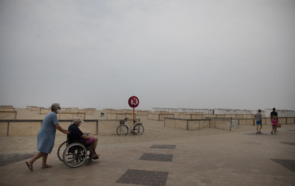 A woman wheels a man in a wheelchair along a part of the beach designated with social distancing markers at the Belgian seaside resort of Knokke, Belgium, Tuesday, Aug. 11, 2020. At the seaside resort of Knokke-Heist, where golf carts with license plates ply well-kept streets, there was ample room to stretch out on the local beach this week. Local authorities have banished day trippers from Belgian cities or France from its 15-kilometer (10-mile) stretch of sands until the heat wave is over. (AP Photo/Virginia Mayo)