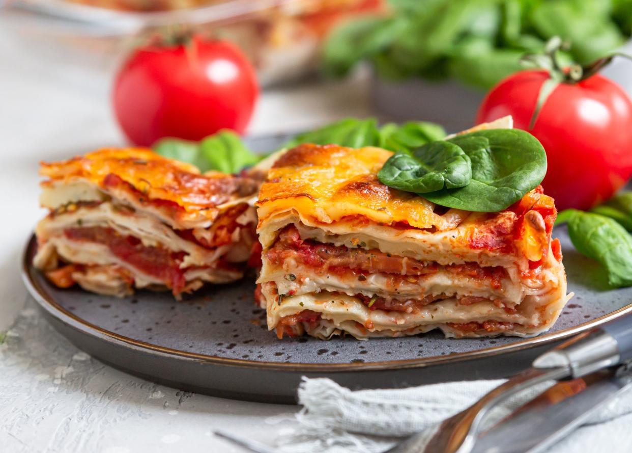 Italian lasagna with tomato sauce and cheese served with tomatoes and spinach, light concrete background. Homemade vegetarian lasagna. Selective focus.