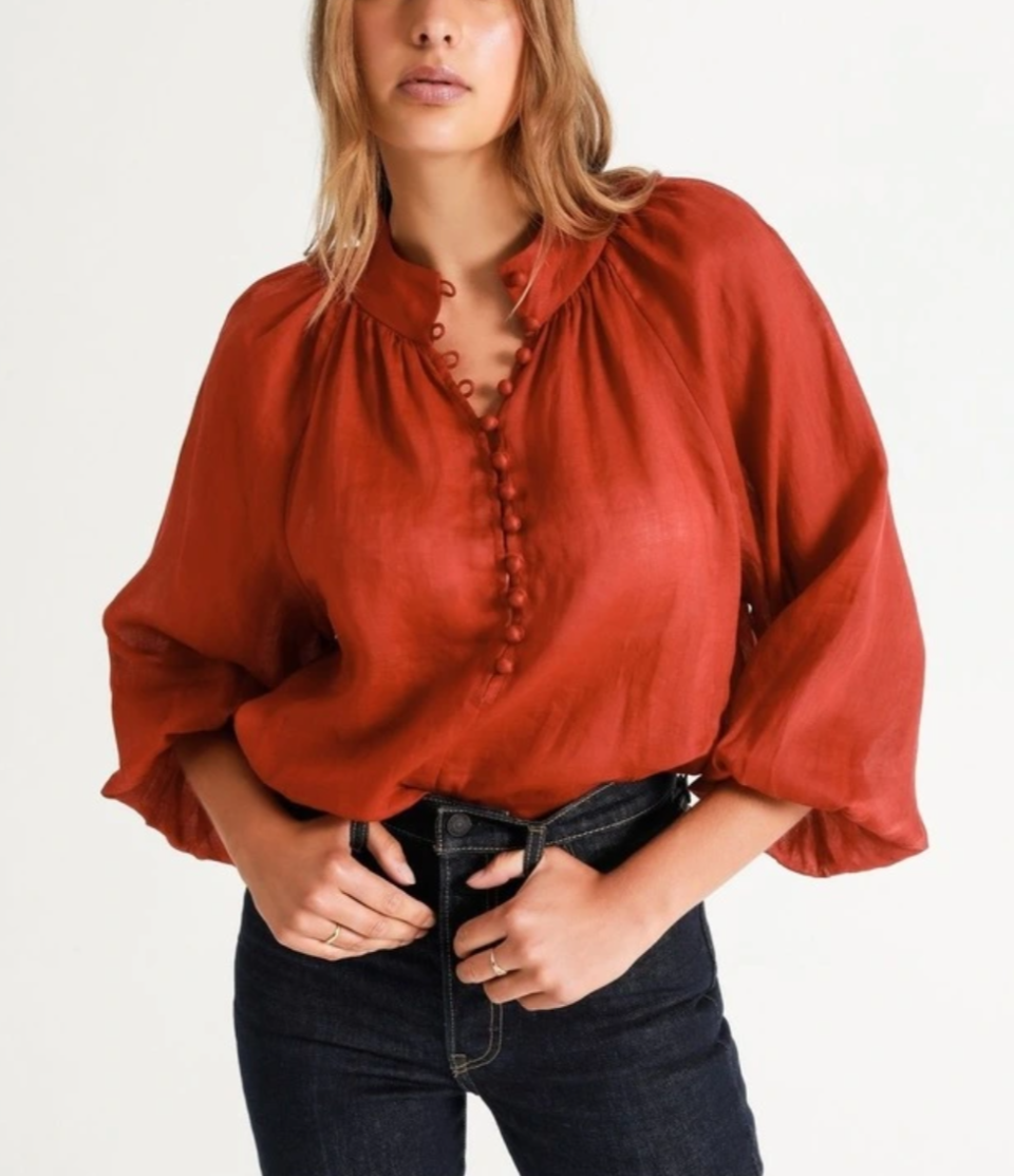 Body of model shown wearing red Piper Ramie High Neck Button Blouse over tight blue jeans.