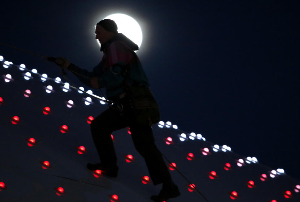 A man's head is silhouetted in the moon as he climbs up the Bolshoy Ice Dome after repairing a light fixture at the 2014 Winter Olympics, Wednesday, Feb. 12, 2014, in Sochi, Russia. 