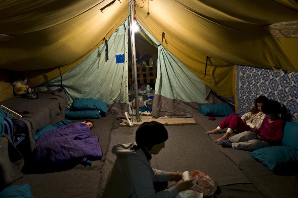 In this Tuesday, Jan. 17, 2017 photo, a Syrian refugee woman works inside her tent while her daughter left lies on the ground and her other daughter play with her friends, in Kalochori refugee camp on the outskirts of the northern Greek city of Thessaloniki. (AP Photo/Muhammed Muheisen)