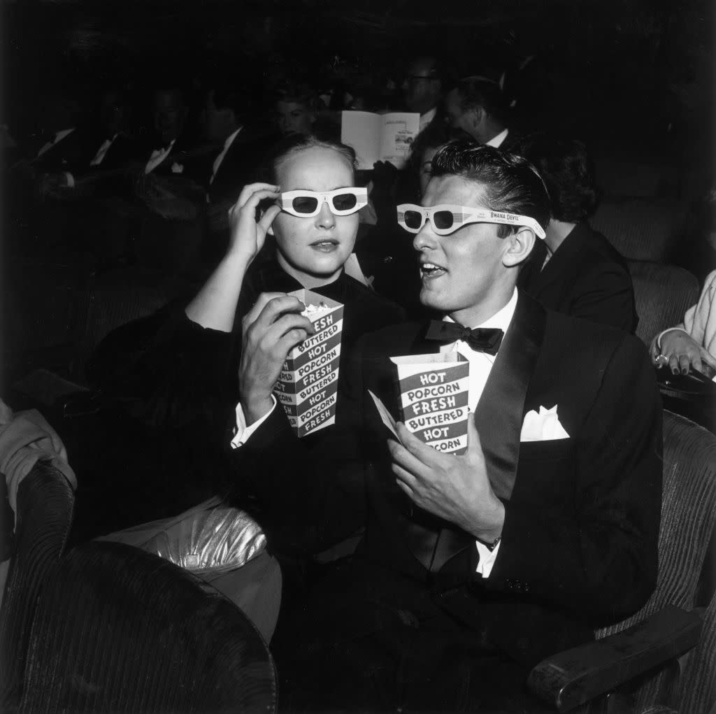 American actor Keefe Brasselle and his wife Norma, wearing 3-D glasses and holding boxes of hot buttered popcorn, sit in the theater at the premiere of director Arch Oboler's film, 'Bwana Devil,' Hollywood, California. The film was the first commercial 3-