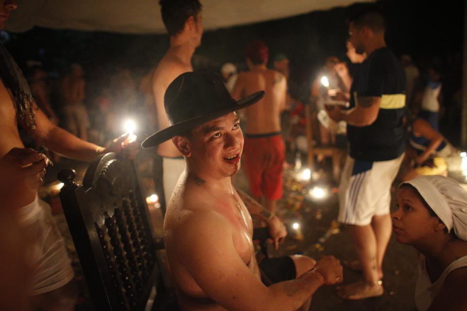 In this photo taken Oct. 12, 2019, a man with chewing tobacco dripping from his mouth goes into a trance as a grandfather spirit known as a "Chamarrero" is believed to enter his body during an annual gathering of followers of indigenous goddess Maria Lionza on Sorte Mountain in Venezuela's Yaracuy state. Those immersed in the old tradition say it puts them in a trance that allows them to channel spirits and escape injury from otherwise dangerous feats. (AP Photo/Ariana Cubillos)