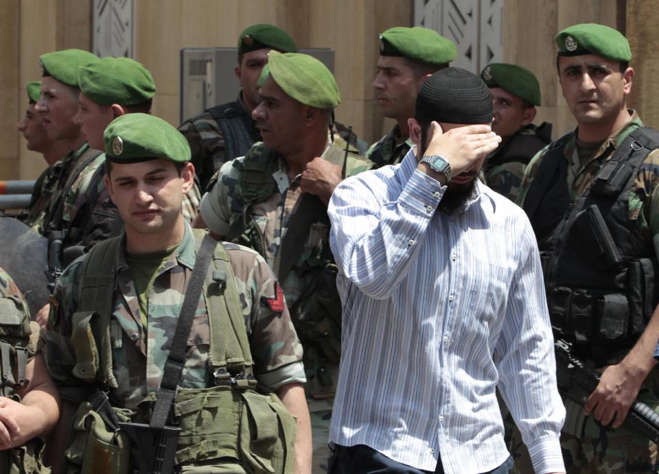 FILE -- In this June 3, 2011, file photo, a supporter of an Islamic group, center, covers his face as he walks among Lebanese army soldiers as he leaves a protest against the Syrian regime inside a mosque, in downtown Beirut, Lebanon. From radical preachers to irreverent taxi drivers, anger is spreading through Lebanon’s Sunni community toward the country’s military, adding a dangerous twist to Lebanon’s instability, already shaken by relentless bombings. Many Sunnis accuse the military of siding with their rivals, the powerful Shiite group Hezbollah, as sectarian tensions grow in Lebanon, stoked by the civil war in neighboring Syria. (AP Photo/Hussein Malla, File)