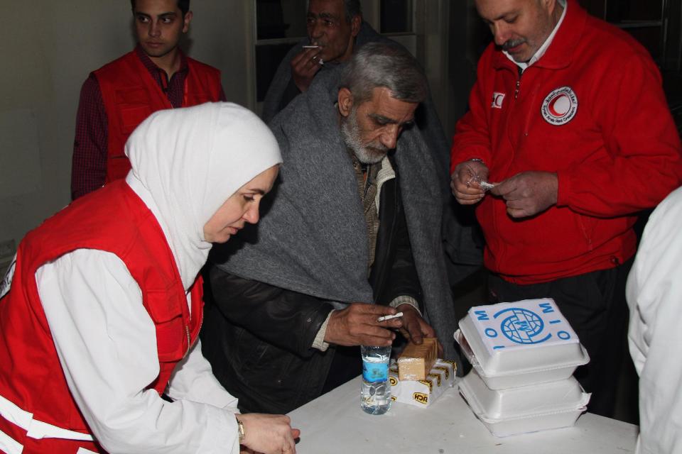 Syrian Arab Red Crescent members in red uniforms provide some food and drink to a man before he gets on a bus to evacuate the battleground city of Homs, Syria, Friday, Feb. 7, 2014. Children, elderly women on wheelchairs and other civilians were evacuated Friday from besieged neighborhoods of Syria's battleground city of Homs under a deal struck between the government and the opposition that also included a three-day cease-fire allowing aid convoys to enter. (AP Photo)