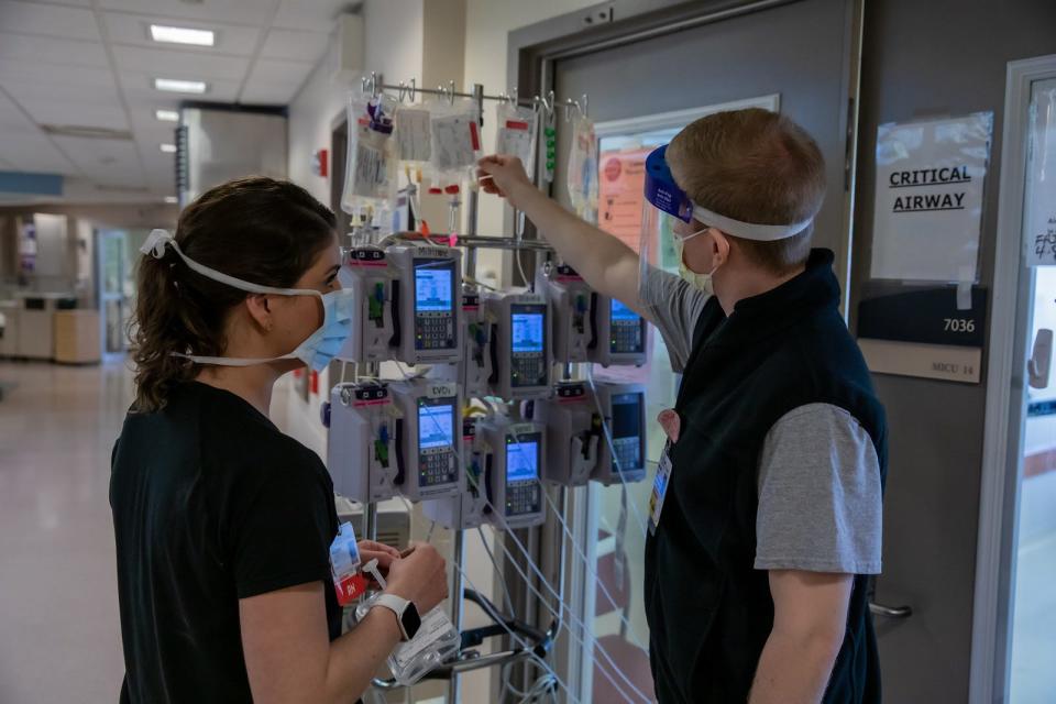 In the medical ICU at the University of Cincinnati Medical Center, two nurses check the stack of intravenous monitors that hang outside the room of a COVID-19 patient. Lengths of tubing deliver the medicine from the pump to the patient .