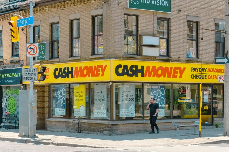 Toronto, Canada, A man walking on a sidewalk alongside a commercial building. Payday Advance Cheque Cash is prominently displayed on the building. (Photo by: Roberto Machado Noa/UCG/Universal Images Group via Getty Images)