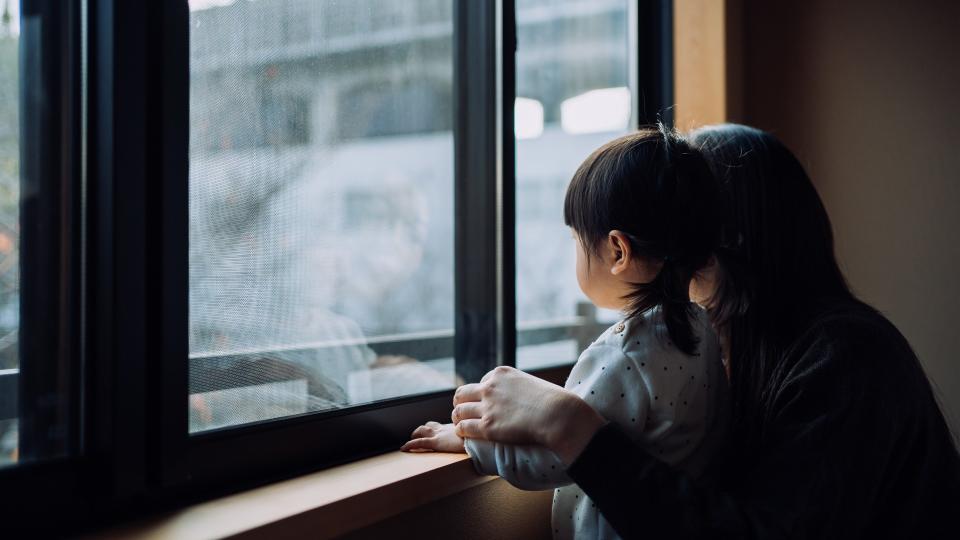 Mother and her young child look out of the window while on self-isolation during the COVID-19 pandemic