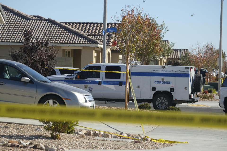 Los Angeles County Coroner vehicle is parked next to a home, left, with a vehicle parked in the driveway, in the city of Lancaster in the high desert Antelope Valley north of Los Angeles, Monday, Nov. 29, 2021. A Los Angeles County Sheriff's Department statement says deputies found a woman, a girl and three boys with gunshot wounds and paramedics pronounced them dead at the scene. The department says the children's father showed up at the Lancaster sheriff's station and was arrested on suspicion of five murders after being interviewed by detectives. (AP Photo/Ringo H.W. Chiu)