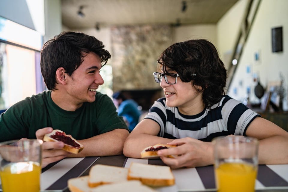 Two people smiling at each other, holding sandwiches at a table with drinks and additional slices of bread