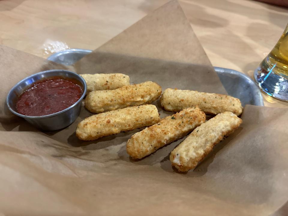 light beige mozarella sticks on parchment paper with metal container of sauce