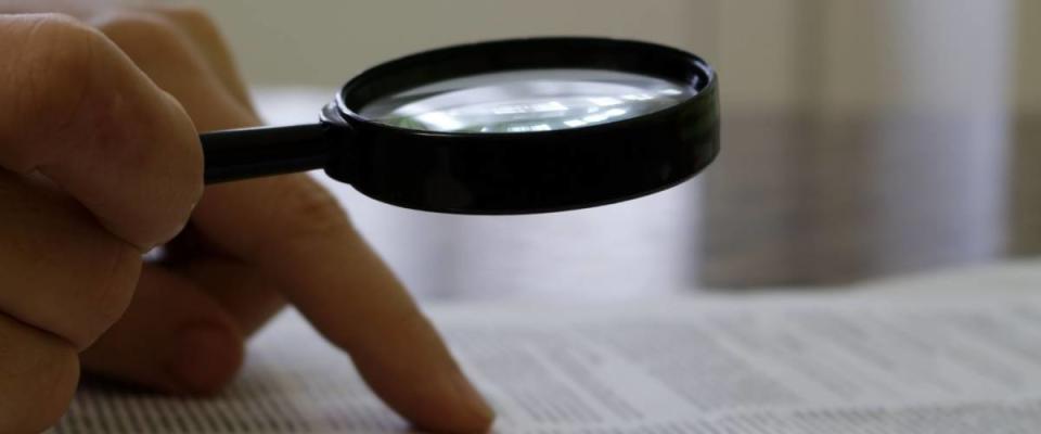 the person reads the document through a magnifying glass at the table