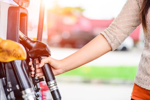 A woman grabbing the handle at a gas pump.