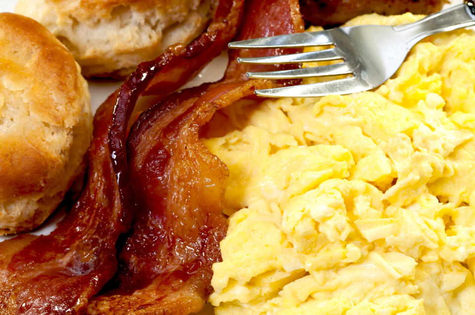 Close-up of scrambled eggs, bacon slices, biscuits, and a fork