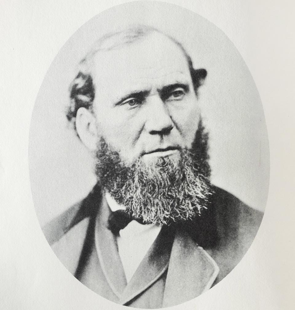 A historical portrait of a man with a full beard, wearing a suit and tie. The image has a vintage style