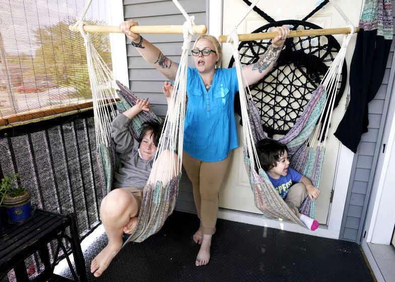 A blond woman plays with two children in swings on a porch of a home.