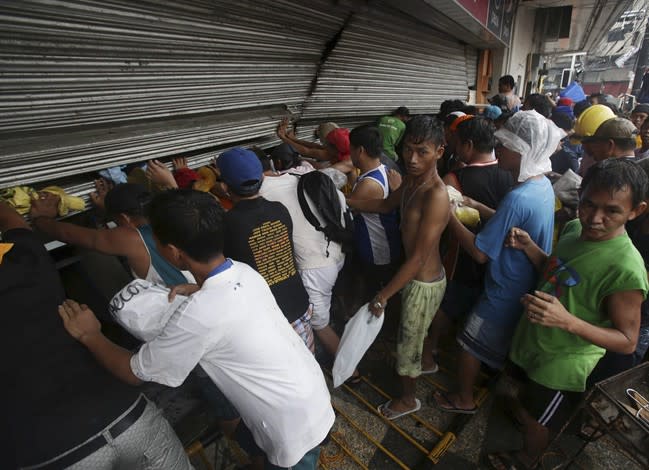 Residents push a shutter to open a small grocery to get food in Tacloban city, Leyte province central Philippines on Sunday, Nov. 10, 2013. The city remains littered with debris from damaged homes as many complain of shortage of food, water and no electricity since the Typhoon Haiyan slammed into their province. (AP Photo/Aaron Favila)