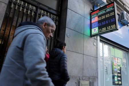 Pedestrians walk past an electronic board showing currency exchange rates in Buenos Aires' financial district