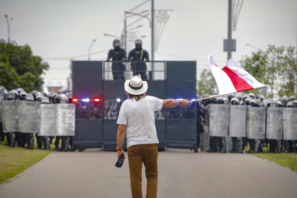 A man waves a historical Belarus flag in front of a riot police blockade during a protest in Minsk, Belarus, Sunday, Aug. 23, 2020. Demonstrators are taking to the streets of the Belarusian capital and other cities, keeping up their push for the resignation of the nation's authoritarian leader, president Alexander Lukashenko, in a massive outburst of dissent that has shaken the country since dubious presidential elections two weeks ago.(AP Photo/Sergei Grits)