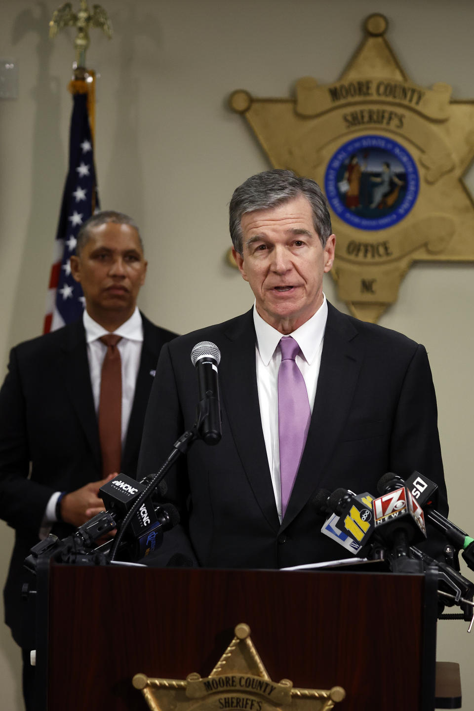 Democratic Gov. Roy Cooper, right, with North Carolina Department of Public Safety Secretary Eddie M Buffaloe, back left, speaks at a news conference at the Moore County Sheriffs Office in Carthage, N.C., Monday, Dec. 5, 2022, regarding an attack on critical infrastructure that has caused a power outage to many around Moore County. (AP Photo/Karl B DeBlaker)