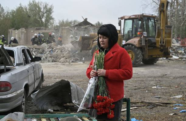 A woman holds flowers as Ukrainian rescuers work to remove debris following a Russian strike which hit a shop and cafe in the village of Groza, some 30 kilometres west of Kupiansk, on 6 October 2023 (AFP via Getty Images)