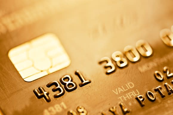 A gold-colored credit card close-up, showing a partial number and the EMV chip.
