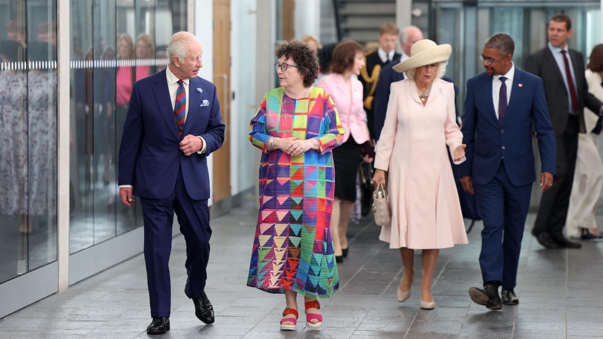 King Charles walking in the senedd foyer chatting with Elin Jones presiding officer, with Queen Camilla and First Minister Vaughan Gething walking behind them 