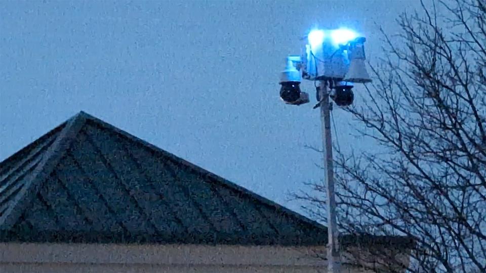 A mast hoisted above the parking lot holds camera and blinking blue lights.