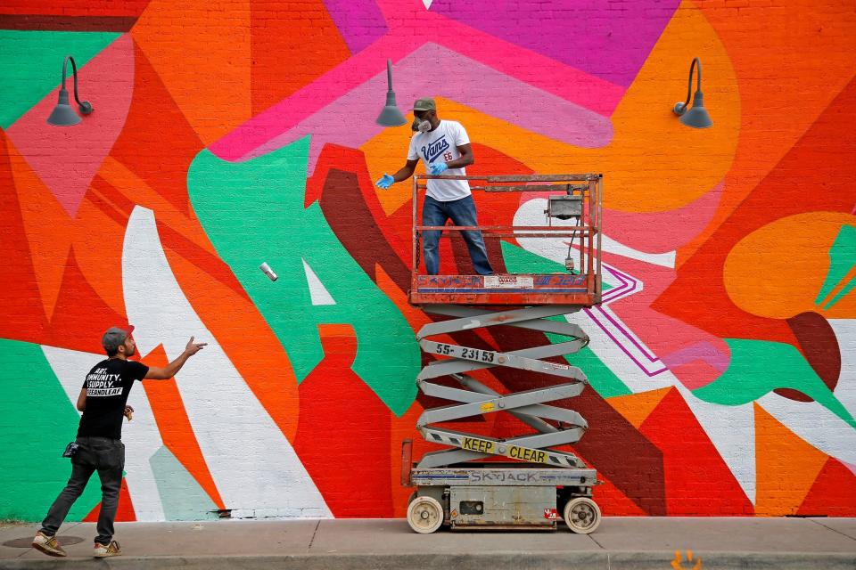 Artist Chris Foxworth, of Kansas City, left, tosses a can of paint to artist Wane Peterkin as he paints the side of a building Sept. 30, 2017, at the Plaza Walls Mural Expo during the Plaza District Festival in Oklahoma City.