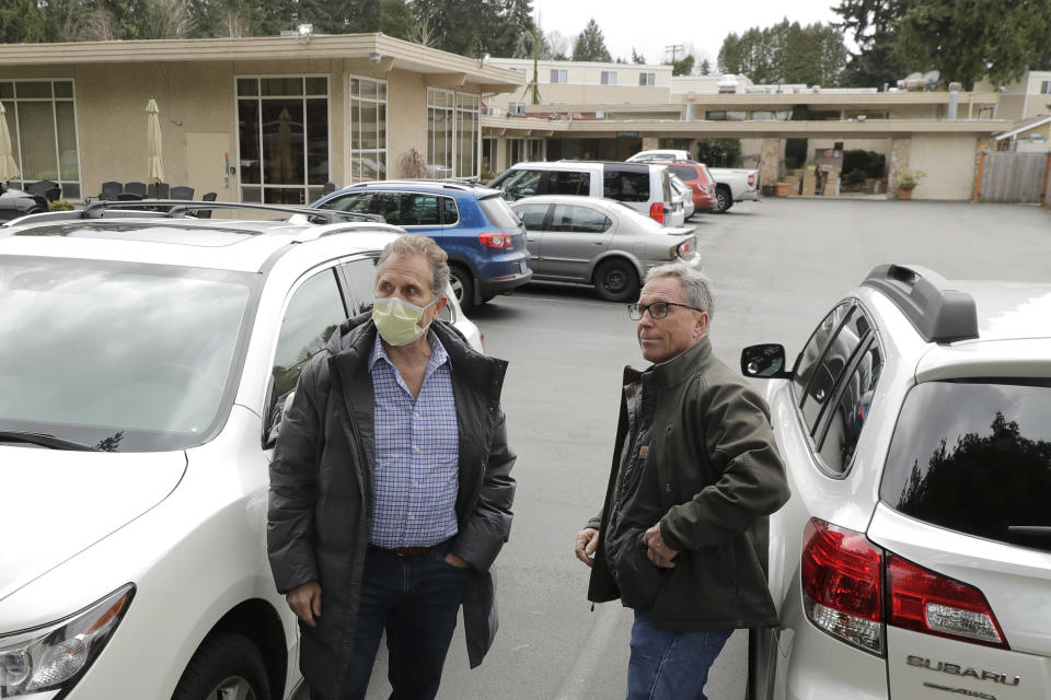 In this March 11, 2020, photo, Scott Sedlacek, left, who has tested positive for the coronavirus, wears a mask as he stands with his brother Steve outside the Life Care Center in Kirkland, Wash. Their father Chuck, who also has tested positive, lives in the facility, which has been at the center of the coronavirus outbreak in the state. Residents of assisted living facilities and their loved ones are facing a grim situation as the coronavirus spreads across the country, placing elderly people especially at risk. (AP Photo/Ted S. Warren)