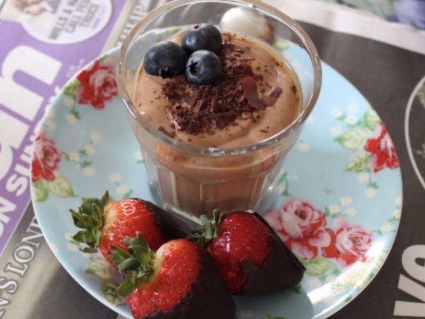 strawberries dipped in dark chocolate alongside a small cup of chocolate mousse with blueberries