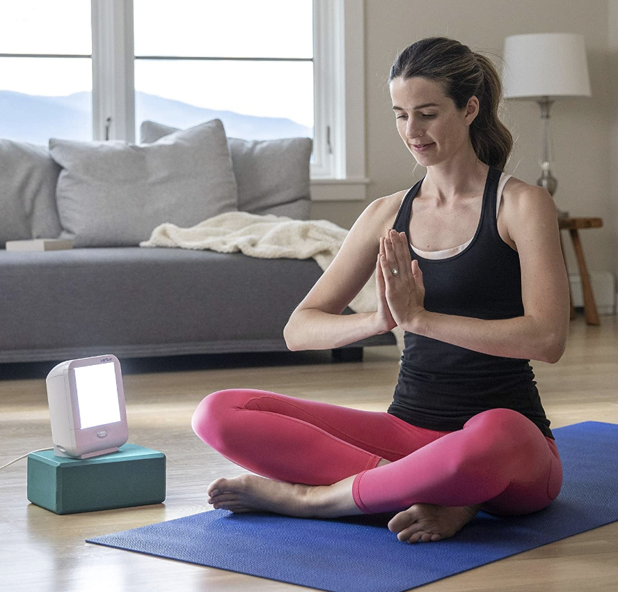 woman doing yoga on yoga mat next to happy lamp, Verilux HappyLight VT10 Compact (Photo via Amazon)