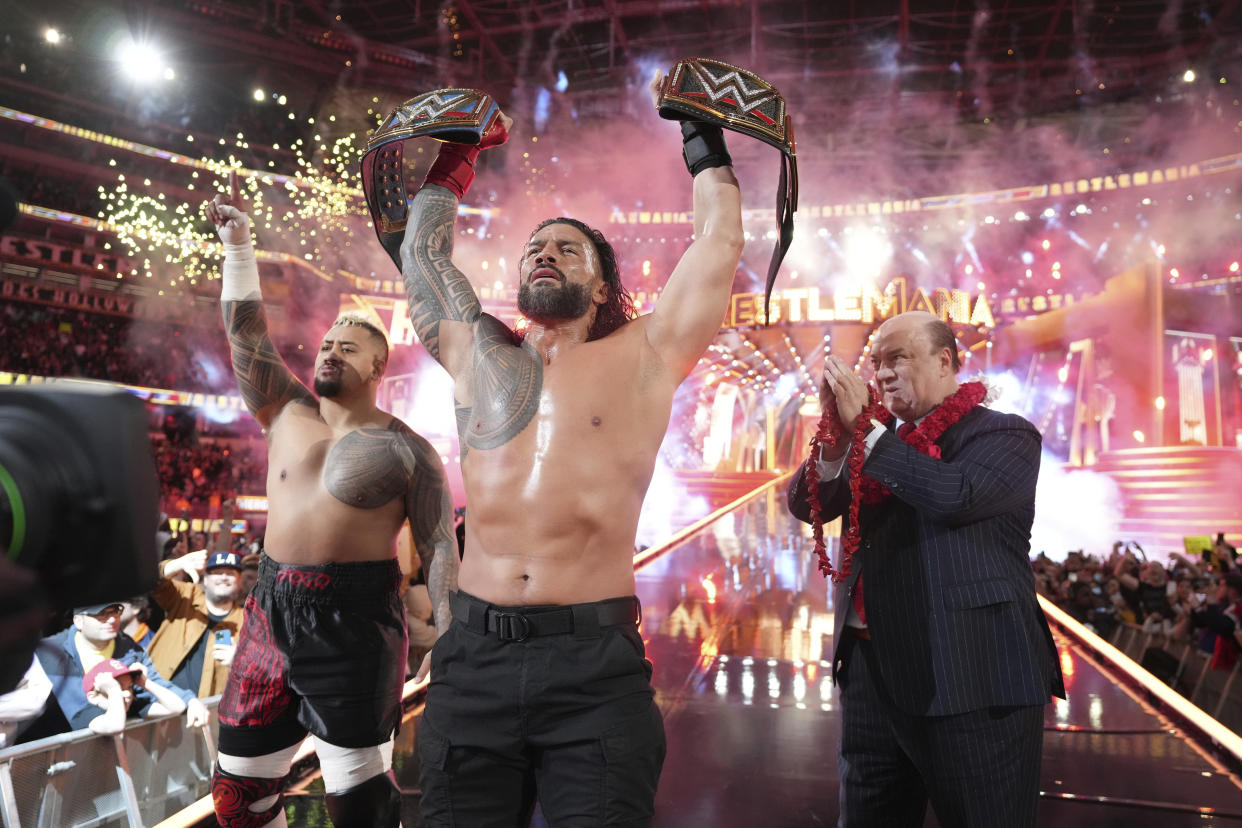 CORRECTS DATE - In this photo provided by WWE, Roman Reigns, center, holds up his WWE heavyweight and universal championship belts after defeating Cody Rhodes in the main event of WrestleMania 39, Sunday, April 2, 2023, at SoFi Stadium in Inglewood, Calif. This was the third straight year Reigns has won the main event. (WWE via AP)