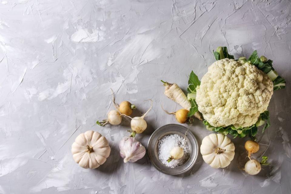 variety of white vegetables raw organic cauliflower, pumpkins, garlic, parsnip and radish with plate of sea salt over gray texture background top view with space healthy eating concept