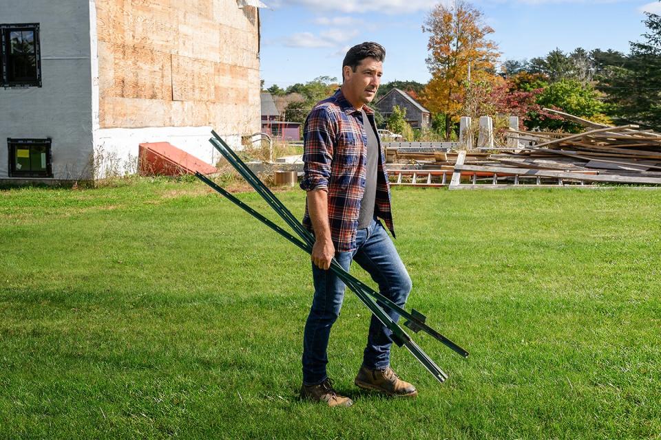 Jonathan Knight walks with fence posts at his New England farmhouse, as seen on Farmhouse Fixer.