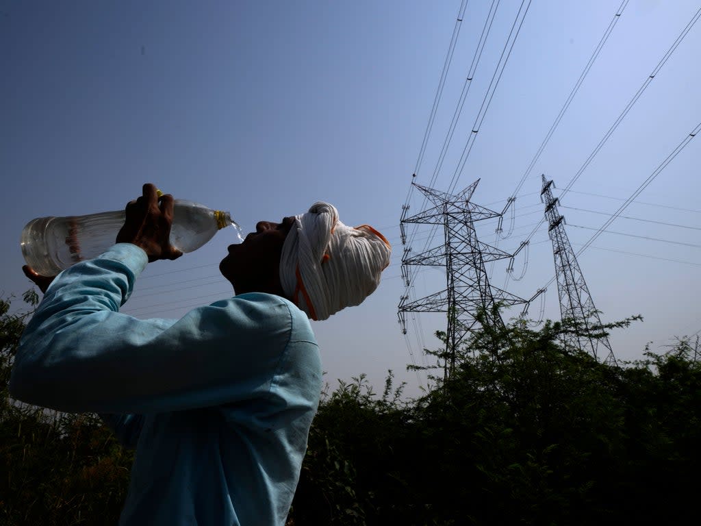 A workers quenches his thirst next to power lines as a heatwave continues to lashes the capital, in New Delhi (AP)
