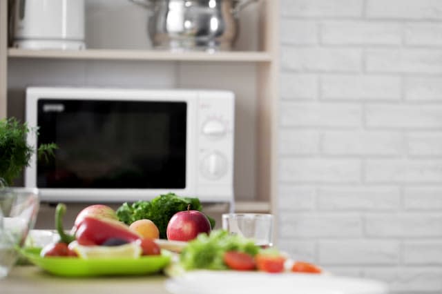 Kitchen view with microwave oven and fresh vegetables and fruit on the table