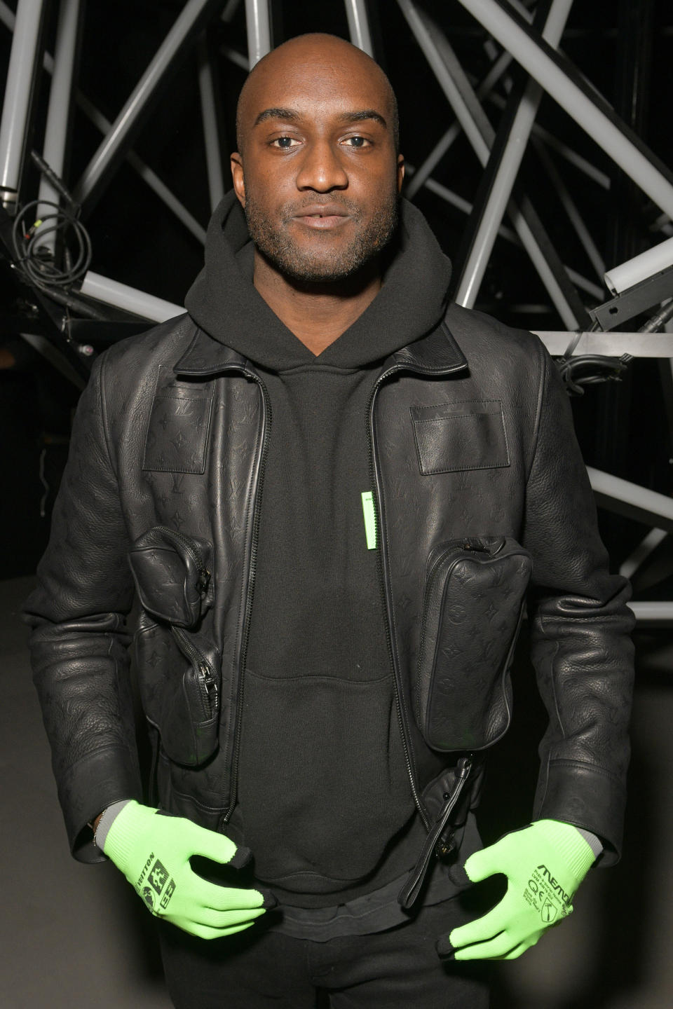 Virgil Abloh wearing a black jacket and hoodie with lime green gloves