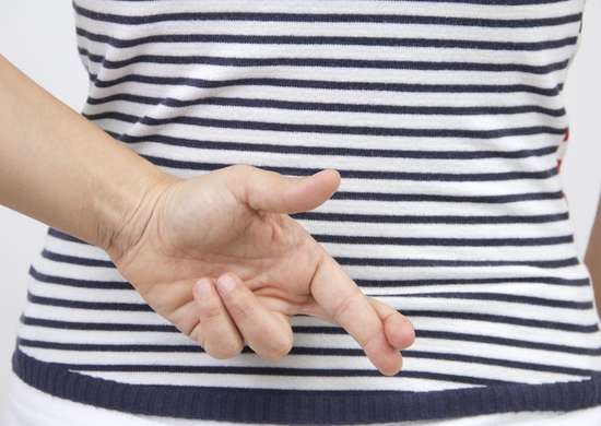 Woman wearing a blue and white striped shirt, crossing fingers behind her back.