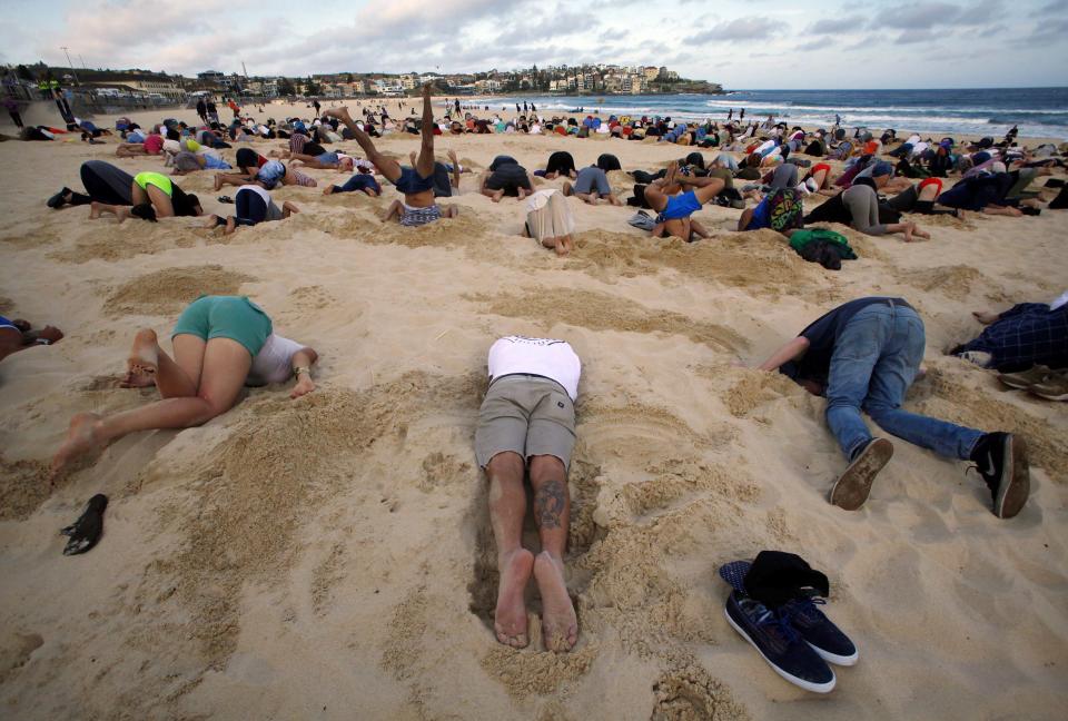 A group of around 400 demonstrators participate in a protest by burying their heads in the sand at Sydney's Bondi Beach November 13, 2014. Hundreds of protesters participated in the event, held ahead of Saturday's G20 summit in Brisbane, which was being promoted as a message to Australian Prime Minister Tony Abbott�s government that, "You have your head in the sand on climate change". REUTERS/David Gray (AUSTRALIA - Tags: POLITICS CIVIL UNREST SOCIETY ENVIRONMENT)