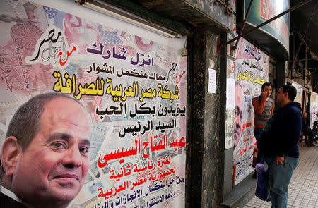 People are seen in front of an exchange bureau, with an advertisement showing images of the U.S. dollar and other foreign currency and a poster supporting Egypt's President Abdel Fattah al-Sisi for the upcoming presidential election in Cairo, Egypt March 14, 2018. REUTERS/Amr Abdallah Dalsh?