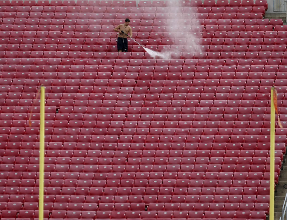 FILE - In this Aug. 7, 2011, file photo, a worker uses a high-pressure hose to clean seats in Papa John's Stadium, in preparation for the upcoming Louisville NCAA college football season in Louisville, Ky. Addressing airborne threats like the novel coronavirus is a particular challenge, especially when they can stick around for hours wherever they might land. (AP Photo/Ed Reinke, File)