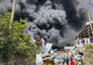 People are seen in front of clouds of black smoke from fires in the aftermath at the scene of an airstrike in Mekele, the capital of the Tigray region of northern Ethiopia Wednesday, Oct. 20, 2021. New airstrikes have hit Mekele, residents said Wednesday, as Ethiopia's government said it was targeting facilities to make and repair weapons, which a spokesman for the rival Tigray forces denied. (AP Photo)